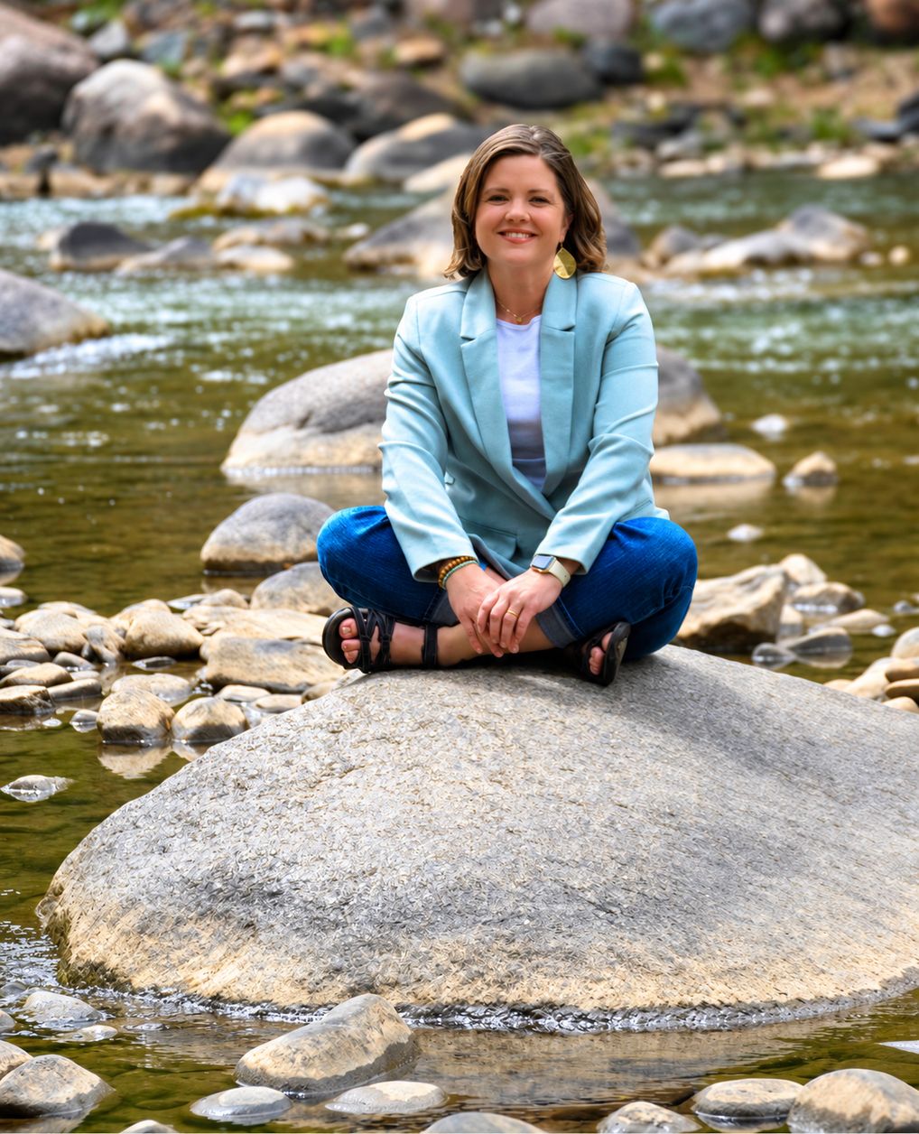 Jodie Miller, LCSW, sitting cross-legged on a rock in the middle of the Animas river